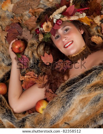 Fall woman with garland of leaves and autumn fruit in her hair lying on a fur blanket