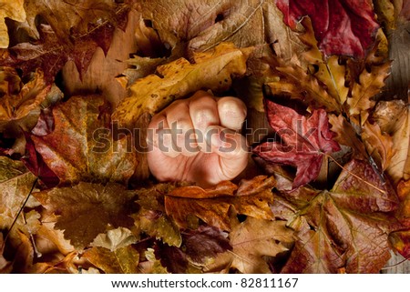 Desperate hand sinking in the ground covered with autumn leaves