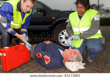 Paramedics putting on sterile gloves to care for a car crash victim  (the sleeve badges have been replaced by a non existing logo)