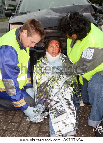 Paramedics putting a protective blanket on a car crash victim (the sleeve badges have been replaced by a non existing logo)