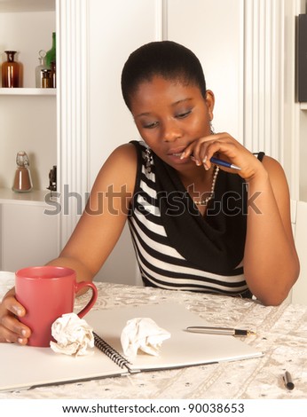 Pensive african woman writing a letter at home