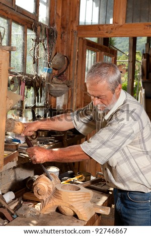 Man working with wood in front of the window of an old derelict shed