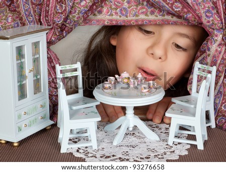 Little girl looking through a window into a doll\'s house like in alice in wonderland