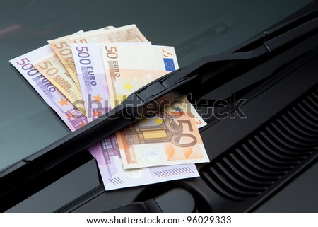 Euros stuck under a windshield wiper symbolizing car expenses