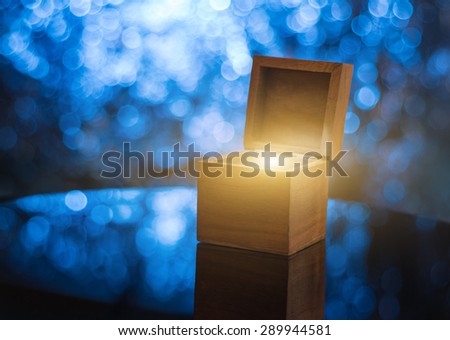 Open wooden gift box with magical light inside, illuminated blue bokeh background