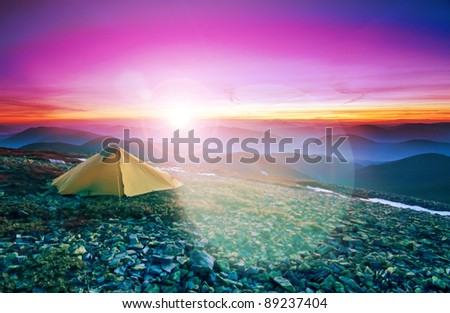 Tourist tent in the rocky mountains and flaring sun on the red horizon