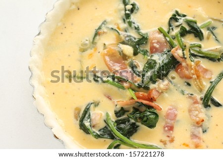 Egg and filling on pie dough for cooing Spinach and bacon Quiche