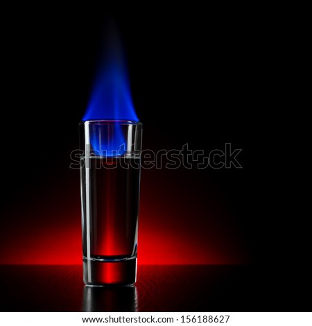 Burning alcohol in shot on a dark red background