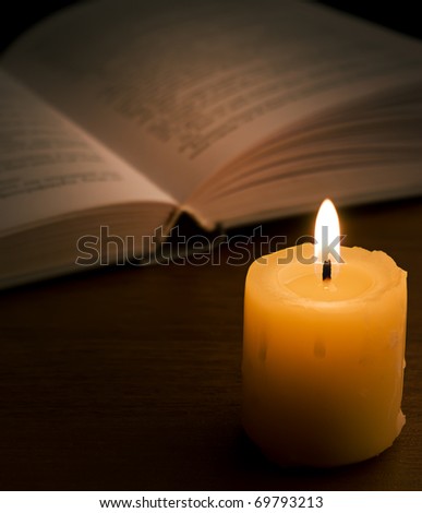Open book and burning candle on dark