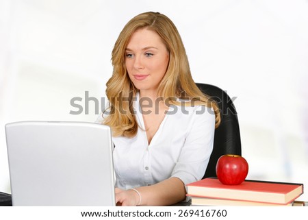 Young teacher with red apple sitting and working on laptop