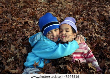 Two small children play around in a pile of leaves