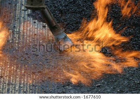 Workers preparing a road for a new tar layer by using a gas burner and rake