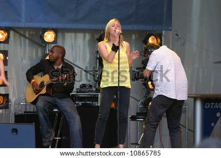 Nicole Appleton from the All Saints performing live on stage with a camera man and a band musician in the background