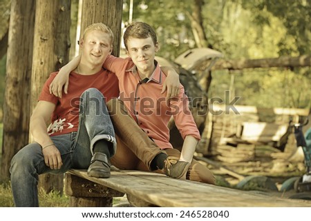 Two friendly male mature students outdoors in park sitting on bench. Two guys hugging