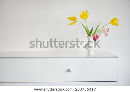 nice interior design scene with a white modern commode and a vase of yellow and pink tulips on a pale grey wall