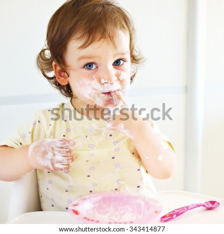 Portrait of eating baby girl with dirty face in high chair