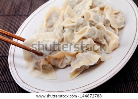Plate of cooked chinese dumplings picked up with chopsticks on bamboo mat