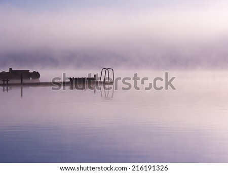 Morning nature foggy misty twilight landscape: fog reflected in water surface along with moorage silhouettes. Can be used as a background or wallpaper. There is empty copyspace to insert a text.