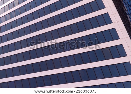 Contemporary architecture concept background: abstract modern business building facade which represents a wall of glass windows reflecting surrounding area and blue sky.