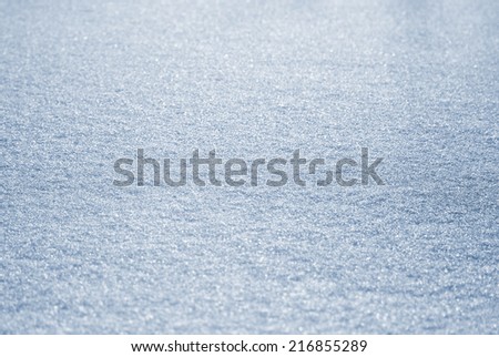 Winter abstract textured background / backdrop with snow surface pattern in white and blue illuminated by sun with light and shadows and snowflakes visible. Can be used as a wallpaper.