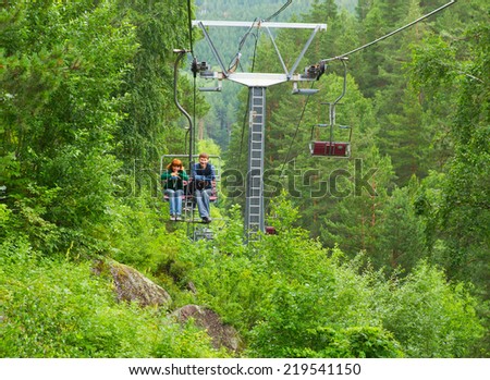 Couple of young hikers or tourists  enjoy the ride of chair lift (ski lift) and the beautiful mountain summer landscape with green trees and plants. Shot was done in the Altai region (Russia).