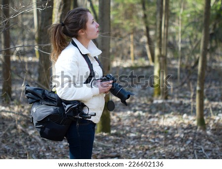 Portrait of nature photographer young woman watching the spring day sunny forest preparing to take images.