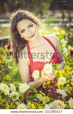 Beautiful young woman  in a garden of roses at sunny summer day