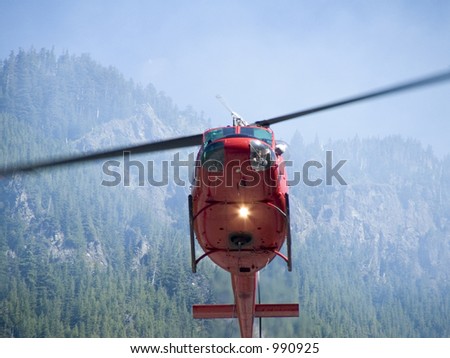 Close up shot of a fire helicopter fighting a forest fire with the pilot looking down watching as he fills his water bladder on a hot sunny day