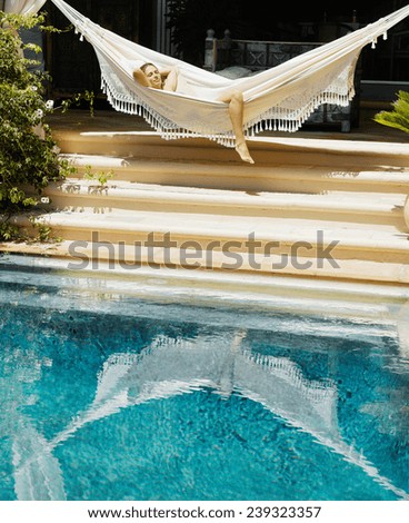 Attractive young woman laying down and relaxing on a white hammock while on vacation in a tropical garden