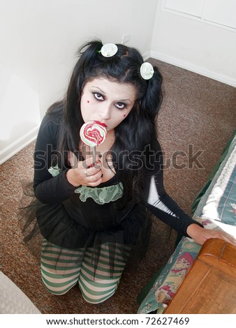 Kneeling young woman performing as a doll with a lollipop