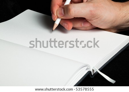 A hand writing with a white pencil on a blank white book (close up)