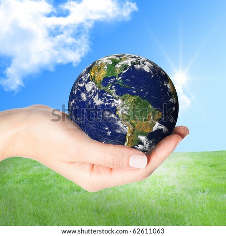 Beautiful female hand holding the Earth against green grass and sunny blue sky