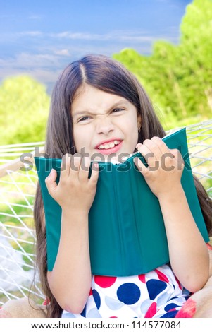 Girl sitting with book on hammock and wrinkles her nose