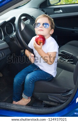 Boy with glasses and red apple sitting in car