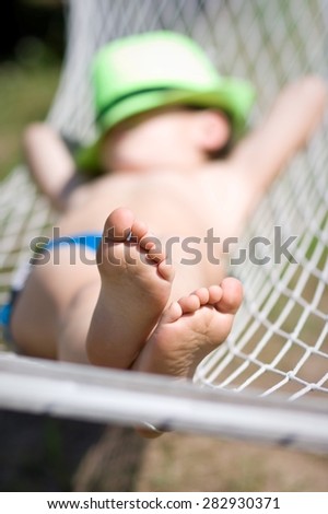 happy boy sleeps in hammock at garden. Focus on feet