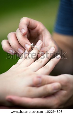 Man placing a diamond engagement ring on the finger of his fiance.  Shallow depth of field with focus on the ring.