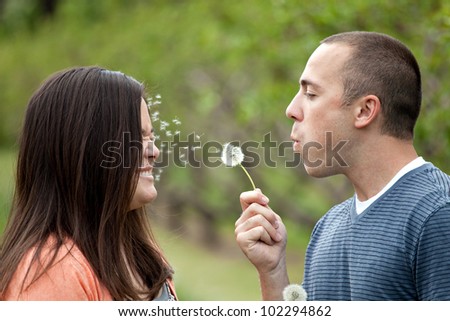 Young happy couple enjoying each others company outdoors.  The man is blowing a dandelion into the face of his girlfriend wife or fiance.