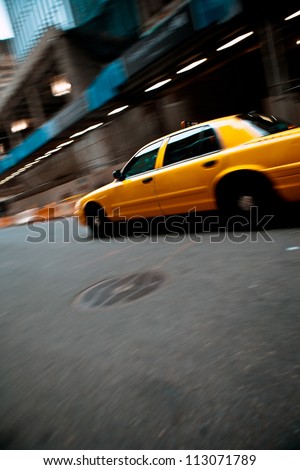 Pnned motion blur of a city street scene with a yellow taxi cab speeding by.