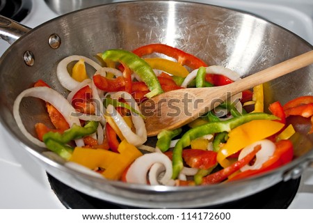 Fresh sliced red green and yellow peppers with onions being stir fried in a stainless steel wok pan. Shallow depth of field.