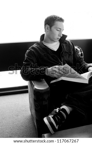 A young college aged man reading a book at the library in black and white.
