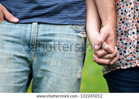 Close up of a young couple holding hands together at waist height. Shallow depth of field.