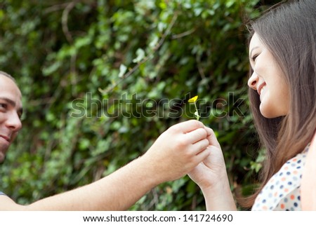 Young happy couple enjoying each others company outdoors.  The man is giving a flower to his love interest.