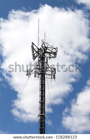 A cellular antenna tower isolated over a blue sky with white fluffy clouds.