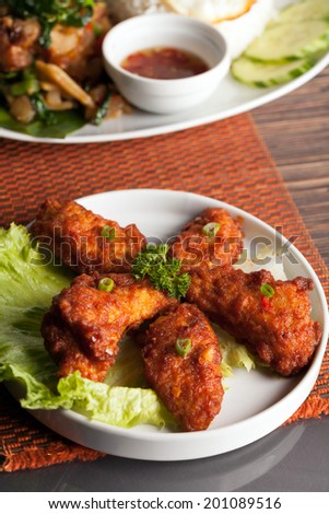 Thai style fried chicken wings on a round white plate with egg noodles and spinach. Shallow depth of field.