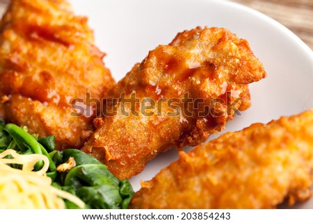 Thai style fried chicken wings on a round white plate with egg noodles and spinach. Close up with shallow depth of field.