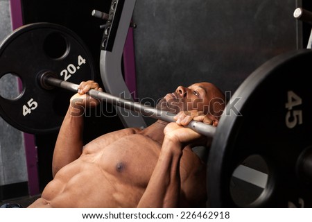 Weight lifter at the bench press lifting a barbell on an incline bench.