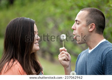 Young happy couple enjoying each others company outdoors.  The man is blowing a dandelion into the face of his girlfriend wife or fiance.
