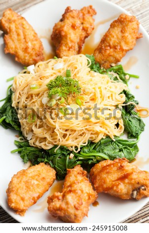 Thai style fried chicken wings on a round white plate with egg noodles and spinach