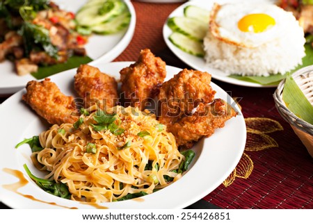 Thai style fried siracha chicken wings on a round white plate with egg noodles and spinach.