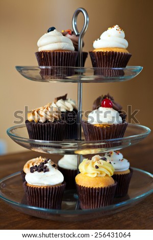 Tiered party serving tray with some decadent gourmet cupcakes frosted in a variety of flavors.